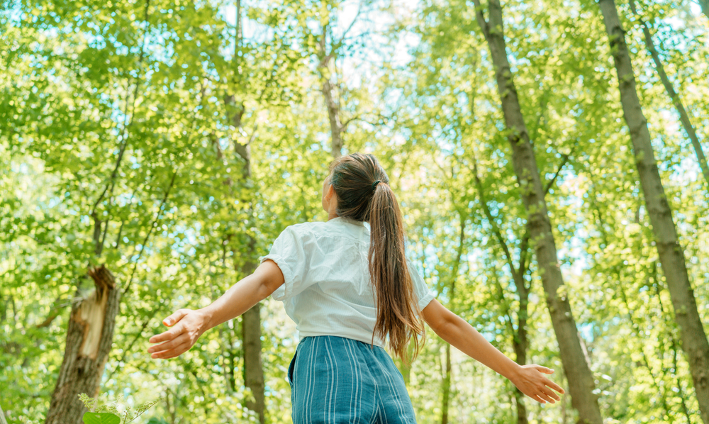 Woman with open arms breathing clean air in nature forest.